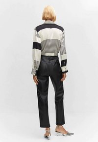 Bluzka w czarno-białe paski z długimi rękawami, zestawiona z wysokim stanem czarnymi spodniami z syntetycznej skóry i błyszczącymi srebrnymi szpilkami. Czysty design.
