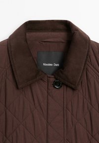 Giacca imbottita marrone con colletto in corduroy, chiusura con bottoni neri e un'etichetta che recita "Massimo Dutti." Tessuto strutturato e caldo.