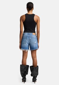 Zwarte geribbelde tanktop, blauwe versleten denim shorts met franje aan de onderkant en zwarte kniehoge laarzen met stippen en hoge hakken.