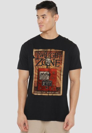 Black t-shirt featuring vintage-style graphic of "The Twilight Zone" with a fortune teller machine, intricate lettering, and muted colors.