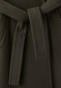 Tmavozelená olivová tkanina s hladkou textúrou. Má vytvorený pás s prekrytými koncami, prešívané detaily a bočné vrecká.