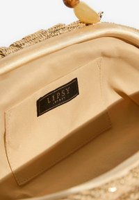 Interiorul unei genți din material auriu cu captuseală de satin netedă, etichetă cu brand în relief și buzunar aplicat. Remarcabil pentru designul său curat.