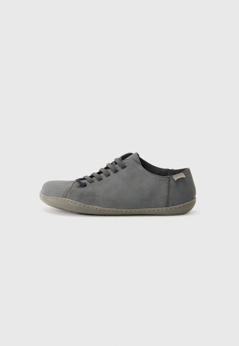 Scarpa casual bassa grigia con chiusura a lacci, suola morbida e piccolo tag in tessuto con il marchio vicino al tallone, mostrata in profilo laterale.