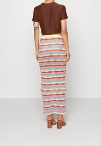 Brun kortärmad t-shirt, färgglad randig stickad maxiskirt med vågor av rosa, blått, gult och brunt. Sandaler med träblockklack.