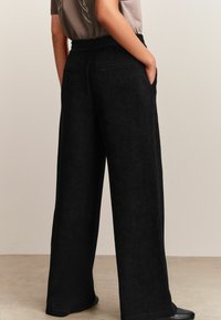 Zwarte corduroy wijde broek met een getextureerde afwerking, voorzien van een hoge elastische tailleband en zijzakken. Soepele stof valt elegant.