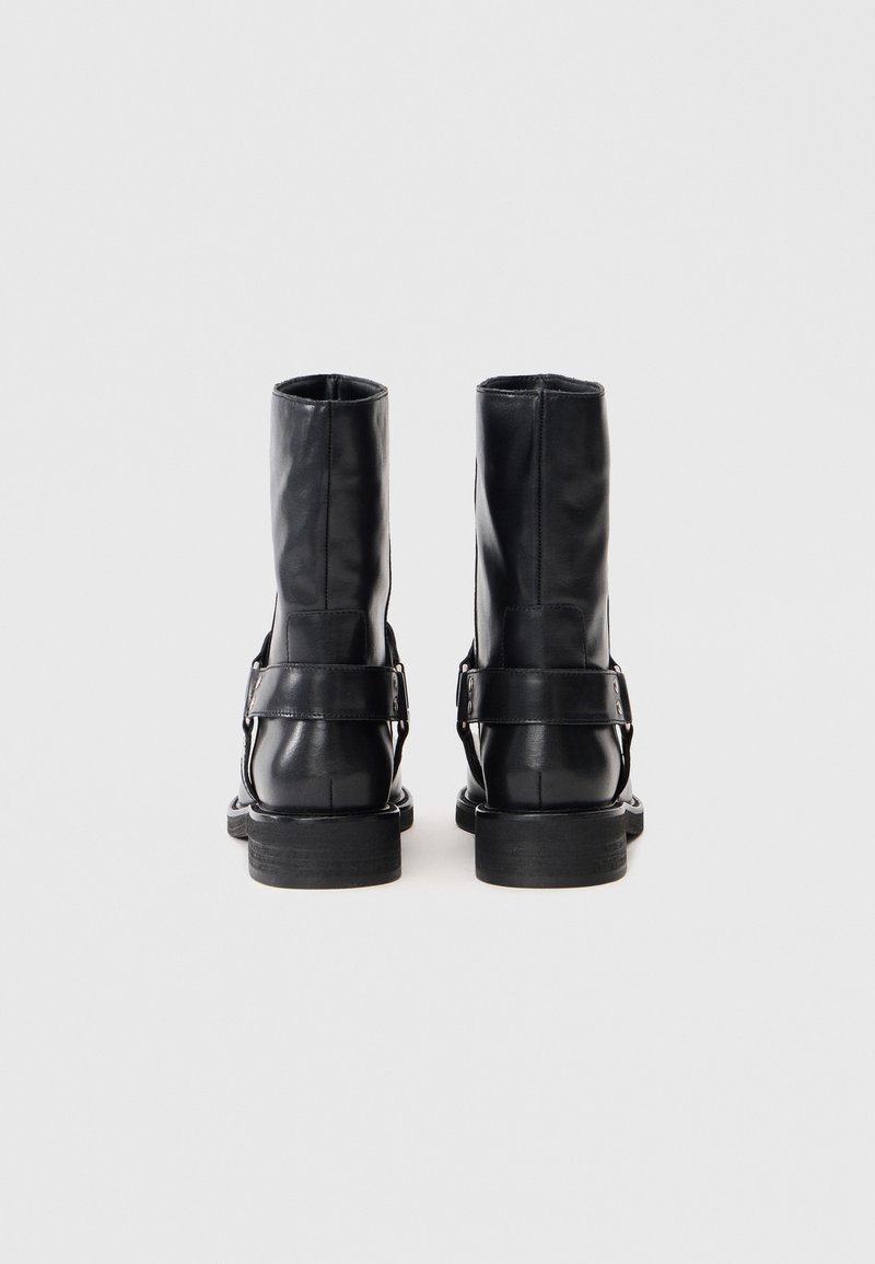 Schwarze Leder-Stiefeletten mit glatter Textur, ausgestattet mit einem Riemen mit Schnallendetail und flacher Gummisohle.