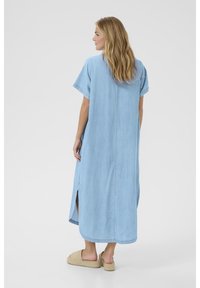 Šviesiai mėlynas džinsinis suknelė su trumpomis rankovėmis, tiesia pudra, šoninėmis plyšiais ir apvaliu hemu. Dėvima su rusvomis espadrilėmis.