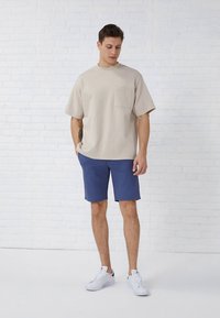 Bež majica s kratkimi rokavi in žepom, kombinirana z mornarsko modrimi kratkimi hlačami. Bele superge zaključujejo priložnostni videz. Gladek material, sproščen kroj.