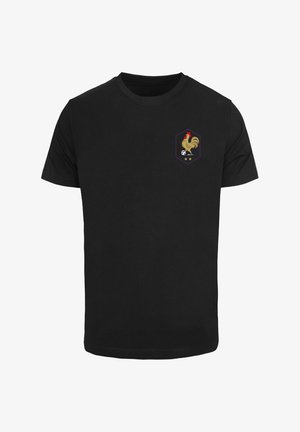 Sort bomulds t-shirt med et hexagonalt emblem, der har en gylden hane, en fodbold og to stjerner i lilla og hvide nuancer.