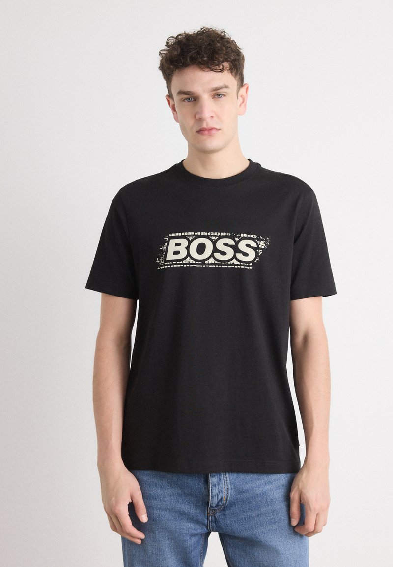 T-shirt en coton noir arborant un audacieux logo "BOSS" blanc, usé, sur la poitrine. Manches courtes et encolure classique.