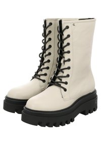Botas de combate con cordones, fabricadas con un cuero texturizado de color blanco roto, cordones negros y una suela de plataforma gruesa negra con un diseño de banda de rodadura resistente.