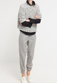 Oversized grå texturerad tröja med svart skjorta under, ihopparat med ljusgrå tapered byxor och vita sneakers.