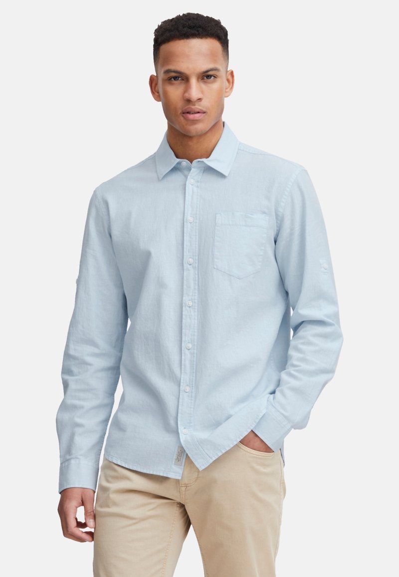 Himmelblaues, langärmliges Hemd mit Knöpfen aus strukturiertem Material, mit einer Brusttasche und hochgeschlagenen Ärmeln, kombiniert mit beigen Hosen.