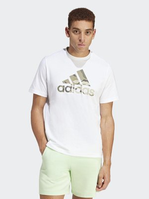 Camiseta blanca de algodón con un gran logo de camuflaje de adidas en dorado. Combinada con pantalones cortos verdes claros, que presentan un diseño sencillo y una textura suave.