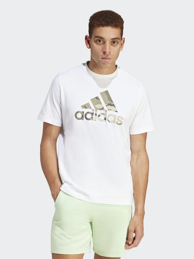 Camiseta blanca de algodón con un gran logo de camuflaje de adidas en dorado. Combinada con pantalones cortos verdes claros, que presentan un diseño sencillo y una textura suave.