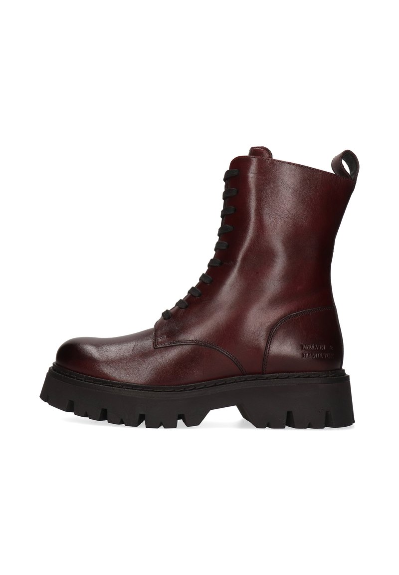 Botín de tobillo de cuero marrón oscuro con cordones y suela de trekking negra gruesa, con tirador en la parte trasera, visto de lado sobre fondo blanco.