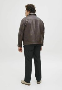Brown leather jacket featuring a classic design with a wide collar and zippered front. Worn with black trousers and light-colored shoes.