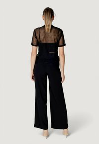 Top negro transparente con mangas cortas, tejido estampado, diseño en capas; combinado con pantalones negros de pierna ancha y zapatos de tacón transparente.
