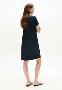 Vestido azul marino de manga corta con un corte relajado, dobladillo a la altura de la rodilla y textura de tela suave. Combinado con sandalias planas de color claro.