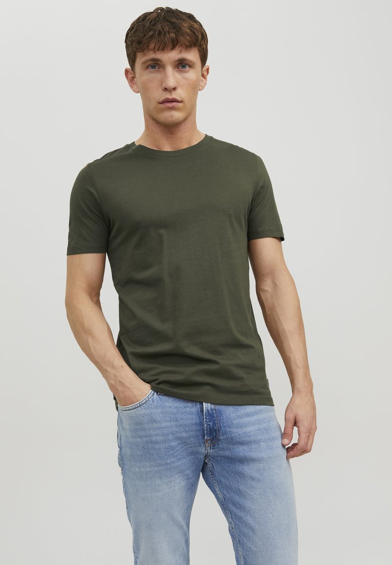 Olivgrünes Baumwoll-T-Shirt mit Rundhalsausschnitt und kurzen Ärmeln, kombiniert mit hellblauen Jeans. Einfaches Design, glatte Textur und figurbetonte Passform.