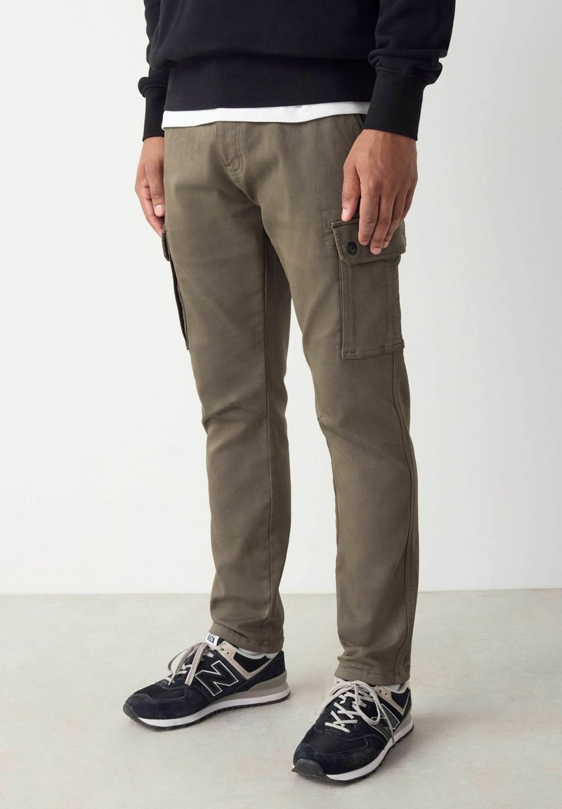 Pantalons cargo kaki ajustés, dotés de poches latérales et d'un tissu robuste. Portés avec des baskets noires et un sweat à capuche noir en couches.
