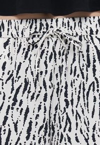 Black and white patterned jogger pants with an elastic waistband and drawstring. Fabric has a smooth texture and features a splatter design.