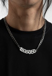 Strieborný náhrdelník s odvážnym pendantom v gotickom štýle "WASTED". Ťažká reťaz má lesklú a hladkú textúru na čiernom tričku.