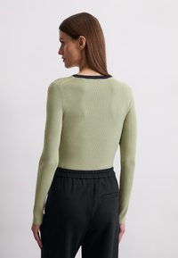 Ribbed long-sleeve top in light green with a black neckline, paired with black pants featuring an elastic waistband and side pocket.