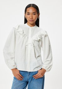Blusa bianca con dettagli arricciati sul davanti, chiusura con bottoni e maniche lunghe. Caratterizzata da un tessuto testurizzato con sottili righe verticali.