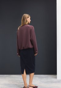 Pull-over bordeaux à manches raglan ; jupe midi noire fendue sur le côté ; porté avec des sandales foncées, sur un fond neutre.