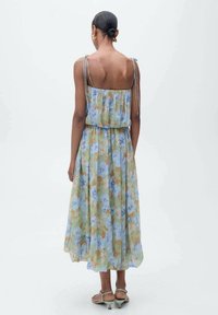 Blumenkleid Maxi mit lockerer Passform, mit blauen und orangefarbenen Blumen auf grünem Hintergrund, dünnen Trägern und einer fließenden Silhouette.