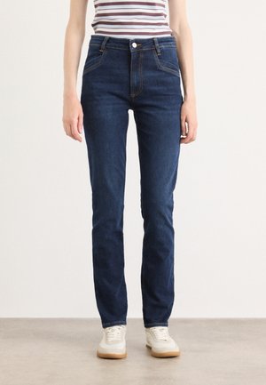 Mørkeblå jeans i rett passform, med høy midje, frontlommer og kontrastsøm. Kombinert med hvite sneakers.