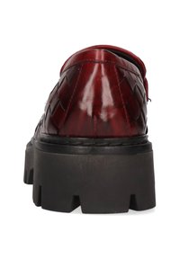 Czerwony tkany skórzany but z połyskującym wykończeniem, zaokrąglonym noskiem i grubą czarną platformą. Charakteryzuje się podniesionym przeszyciem wzdłuż szwów.
