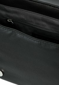 Interno di una borsa in pelle nera con una superficie testurizzata, dotato di una tasca con zip e rivestimento liscio. Dettagli in metallo argentato visibili.