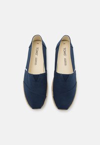 Scarpe slip-on in tela blu navy con finitura testurizzata, dotate di una suola in juta intrecciata e un'accenno cucito a forma di V nella zona delle punte.