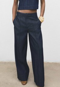 Pantalons larges en denim foncé avec une taille haute, des poches avant, des coutures visibles et une texture lisse, associés à un haut court assorti.