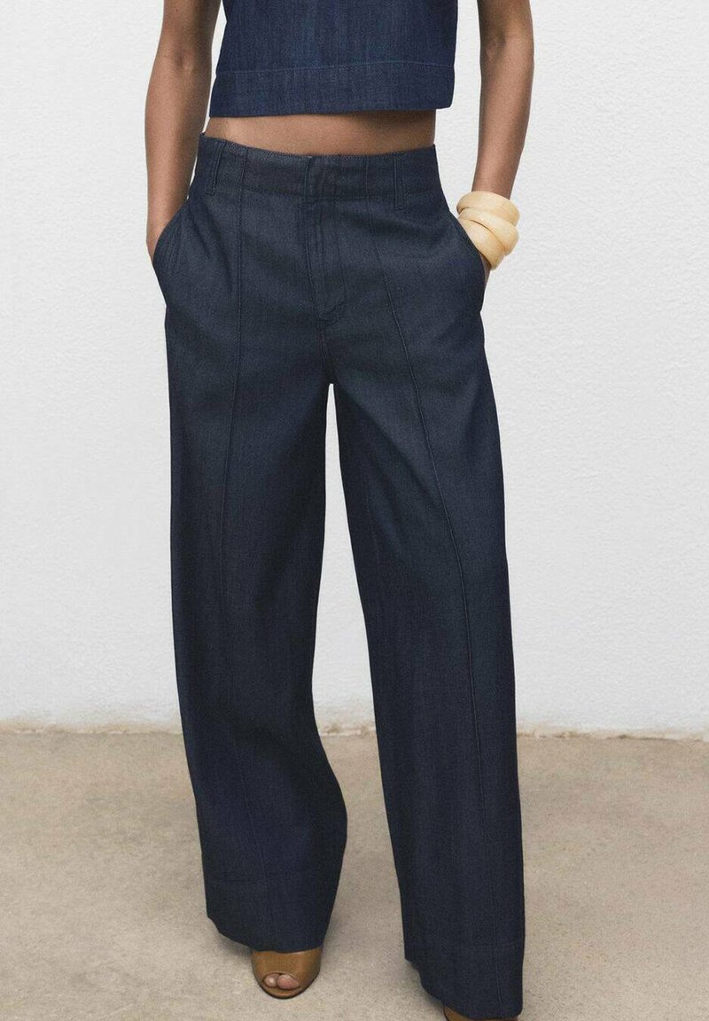 Pantalons larges en denim foncé avec une taille haute, des poches avant, des coutures visibles et une texture lisse, associés à un haut court assorti.