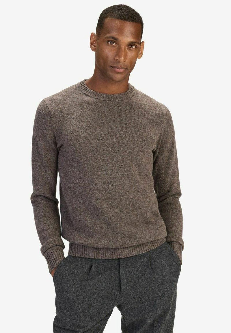 Brun rundhalsad tröja i en texturerad stickning. Långa ärmar med ribbade manschetter och nederkant, parat med mörkgrå byxor.