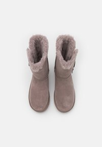 Un par de botas de invierno de ante taupe con forro de peluche, vistas desde arriba sobre un fondo blanco liso.