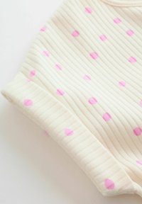 Tissu crème côtelé avec un poignet élastique, décoré de petits pois roses dispersés.