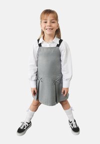 Harmaa mekko mustilla olkaimilla, laskostettu muotoilu ja nauhakoristeet. Vuosia valkoisen pitkähihapaidan päällä. Yhdistetty mustien lenkkareiden ja valkoisten sukkien kanssa.