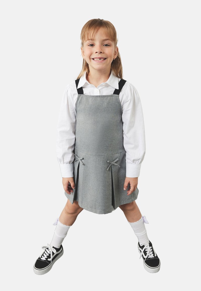 Harmaa mekko mustilla olkaimilla, laskostettu muotoilu ja nauhakoristeet. Vuosia valkoisen pitkähihapaidan päällä. Yhdistetty mustien lenkkareiden ja valkoisten sukkien kanssa.