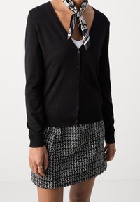 Svart cardigan med v-ringning, framknäppning och långa ärmar. Kombinerad med en minikjol med texturerat svart och vitt mönster.