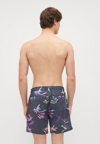 Čierne plavkové šortky so živým tropickým vzorom listov v ružovej, zelenej a modrej farbe, s elastickým pásom a vo voľnom strihu.