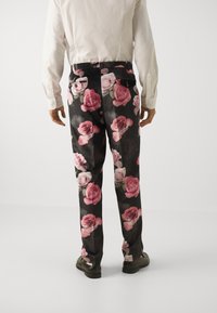 Floral trousers with a black base featuring large pink and white rose patterns. Made from a smooth fabric, with back pockets and a fitted design.