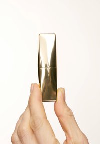 Gullfarget leppestiftetube holdt oppreist, med et elegant rektangulært design med en reflekterende overflate og uten synlig merkevare eller detaljer.