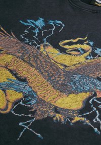 T-shirt noir avec un graphique coloré d'aigle et le mot "Superdry" en lettres jaunes épaisses et accents bleus, détails d'impression texturée.