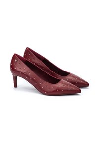 Zapatos de tacón alto de cuero sintético rojo con un diseño de punta afilada, que presentan pequeñas tachuelas plateadas y un tacón de 3 pulgadas.