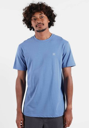 T-shirt en coton bleu clair à manches courtes, col rond, avec un petit logo blanc sur la poitrine gauche. Texture lisse, coupe décontractée.