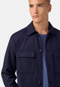 Námořnický kabát z vlněné směsi s knoflíkovou légou, dvěma náprsními kapsami a klasickým límcem. Hladká textura, přiléhavý střih, ideální pro vrstvení.